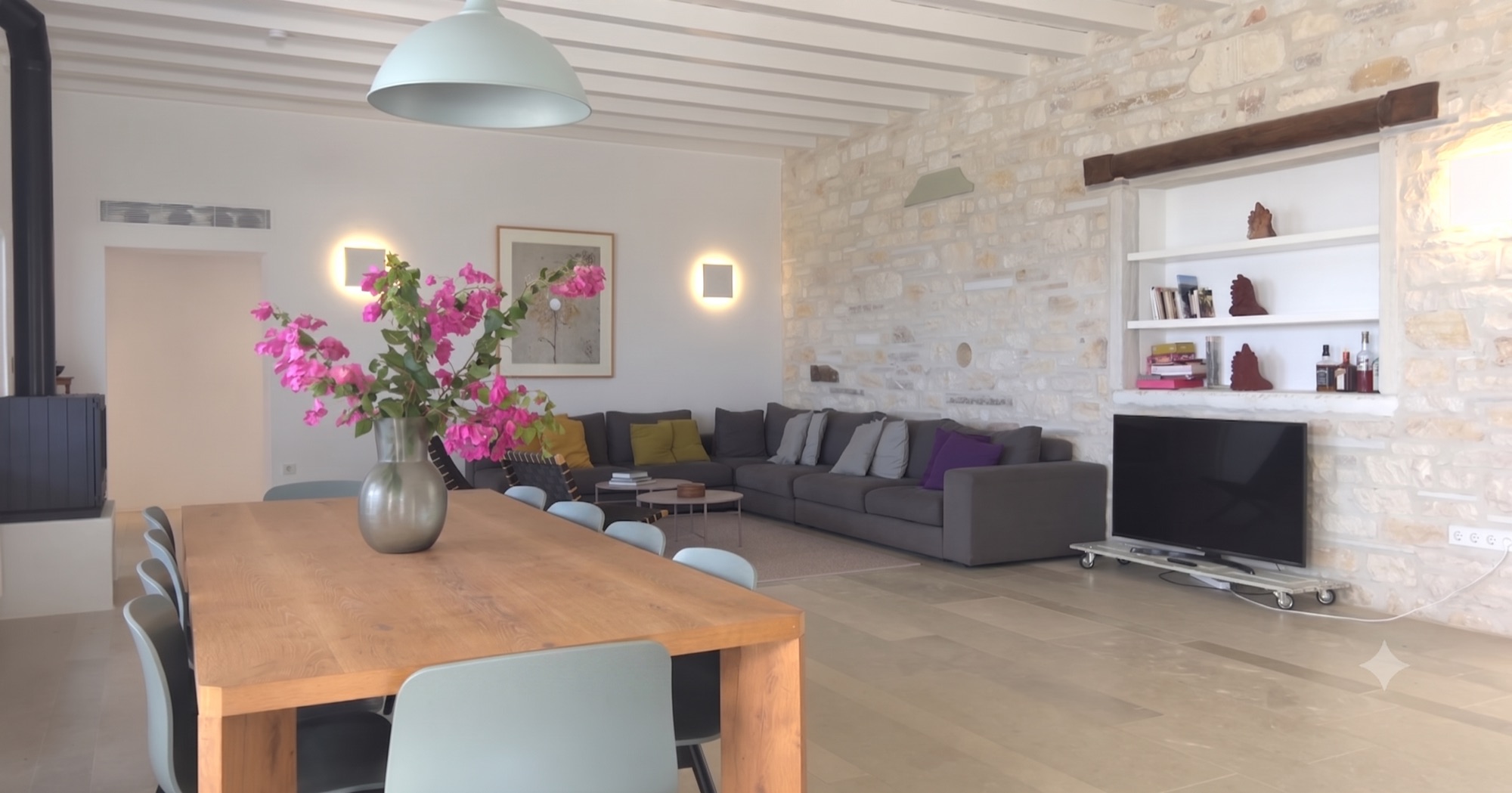 The living room, wood-beamed ceiling and stone wall, with the dining table